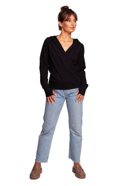 BeWear Elegant Sweatshirt With Hood, designed with a slim fit and thumb cutouts, displayed on a model in a chic black sweatshirt. The crossover front adds a touch of unique elegance, complemented by casual denim.