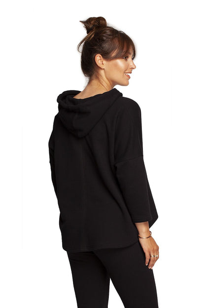 Side profile of the BeWear Loose-Fitting Trapeze Sweatshirt in Soft Knit with Hood and Faux Leather Accents in black, emphasizing its luxurious texture and contemporary design.