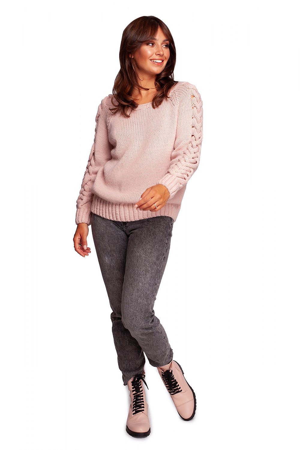Full view of model in luxury fitted jumper with shoulder revealing neckline in light pink, complemented by grey jeans and fashion boots.