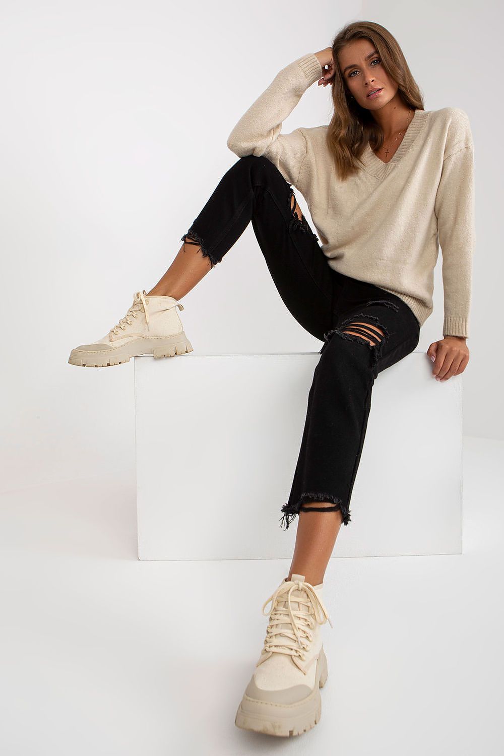 Elegant Women's Long Sleeve Sweater with Heart Neckline by Rue Paris - A fashionable pose of a model wearing the beige sweater, paired with distressed black jeans for a contemporary look.