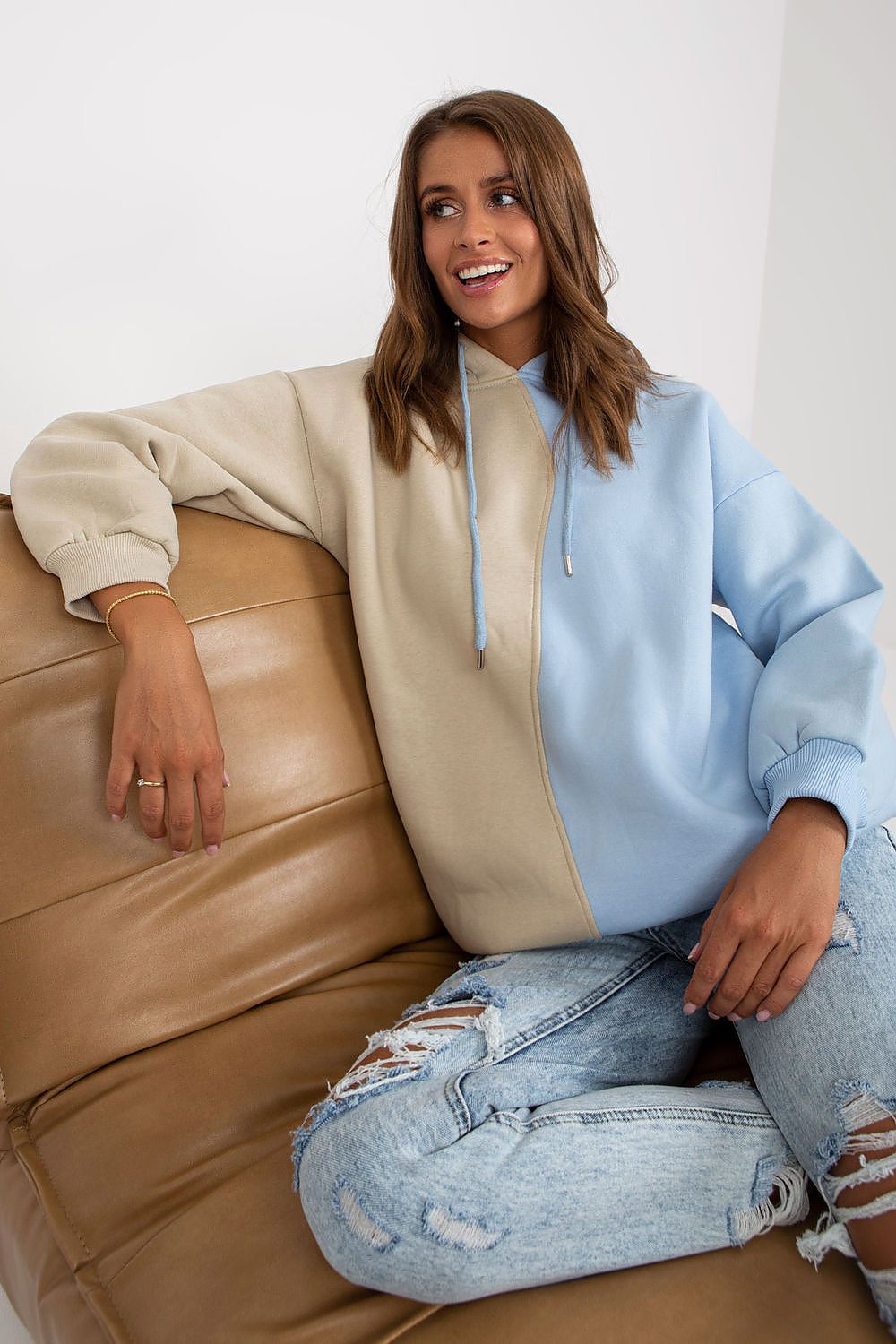 Relaxed pose of a model in the Luxurious Two-Colour Women's Hoodie Sweatshirt by Rue Paris, seated on a stylish couch, showing off the trendy design.
