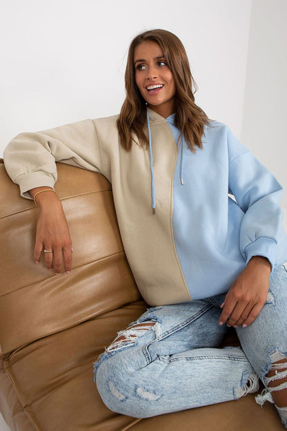 Relaxed pose of a model in the Luxurious Two-Colour Women's Hoodie Sweatshirt by Rue Paris, seated on a stylish couch, showing off the trendy design.