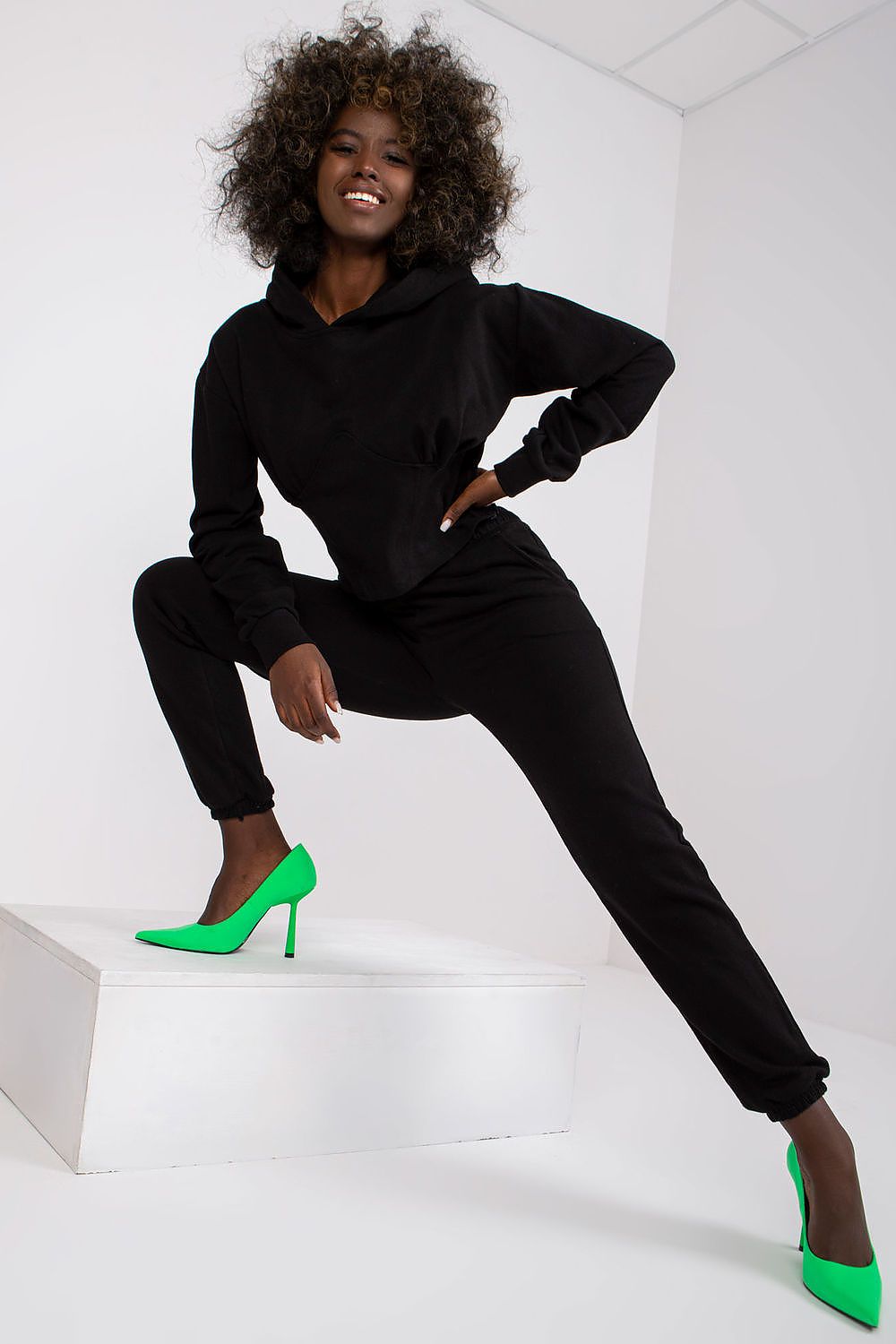 Luxury Ex Moda Cotton-Blend Sweatshirt Set with Corset Insert & Elastic Waist Pants worn by a model, showcasing the stylish black hoodie and matching pants, accentuated with vibrant green heels.
