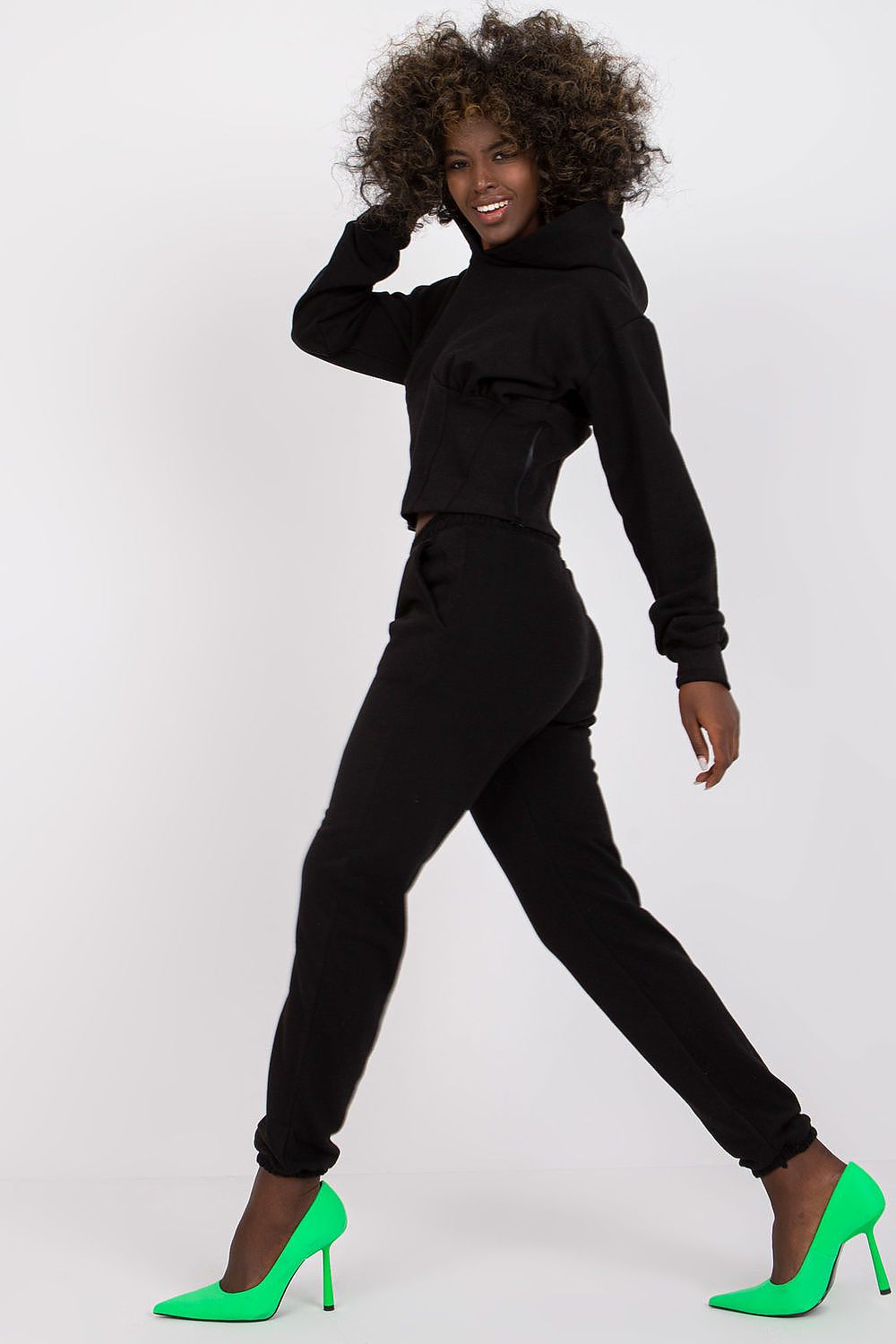 Luxury Ex Moda Cotton-Blend Sweatshirt Set with Corset Insert & Elastic Waist Pants displayed by a model, highlighting the elegant black crop sweatshirt with hood and elastic waist pants, paired with bright green heels.