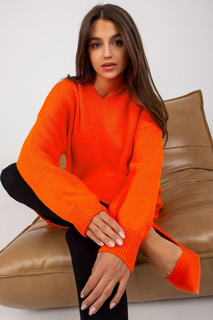 Luxurious Rue Paris Women's Sweater with Extended Cut, Long Sleeves and Heart Neckline, showcased in a vibrant orange colour, styled on a model seated on a chic sofa, perfect for adding a pop of colour to your wardrobe.