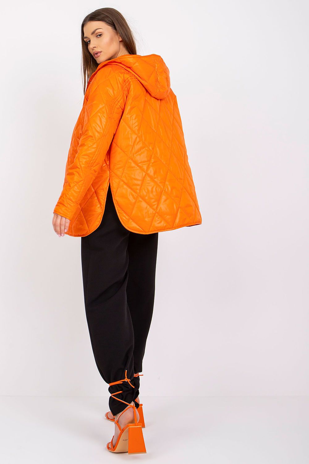 Effortlessly stylish in the Women's Quilted Hooded Jacket by Rue Paris, seen from the back. The model displays the luxurious quilted design and vibrant orange colour, ideal for those looking for trendy, transitional outerwear.