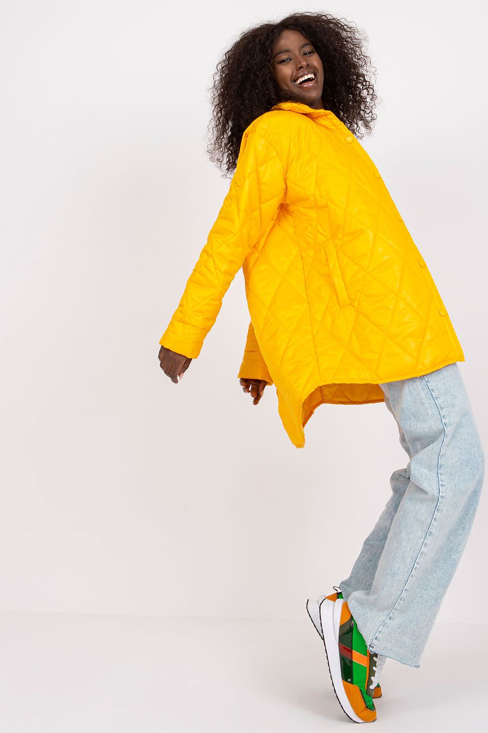 Joyful pose of a woman in the Elegant Women's Quilted Jacket by Rue Paris, bright yellow and designed for long sleeves, paired with trendy sneakers, illustrating a fashionable and elegant style.