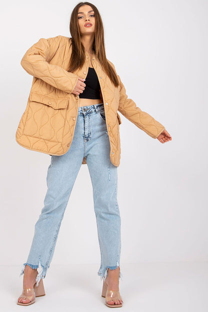 Rue Paris Women's Quilted Transitional Jacket in a warm camel hue, featuring long sleeves and large pockets, exemplified by a model dressed in a cropped black top and distressed jeans.