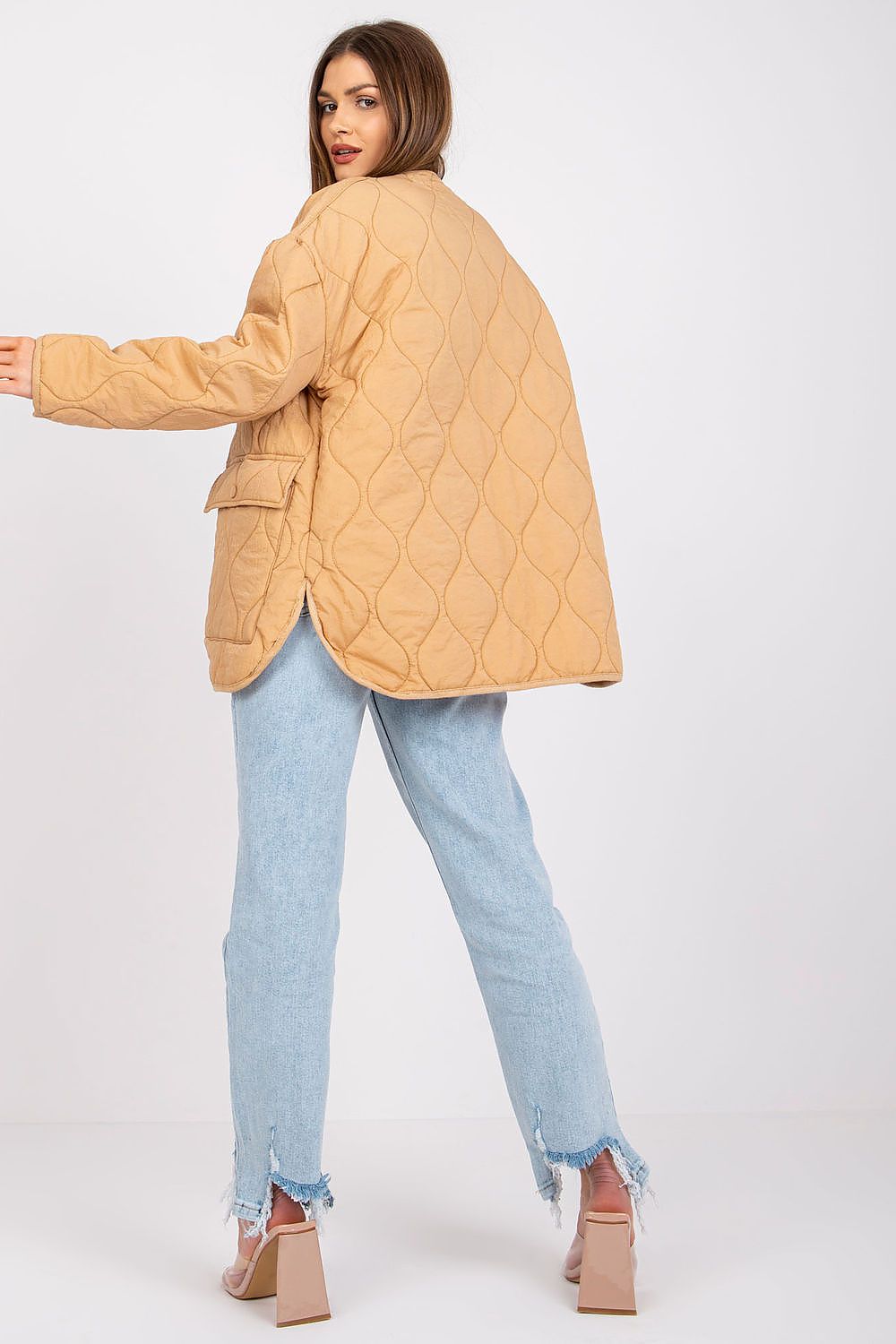 Rear view of the Rue Paris Women's Quilted Transitional Jacket in camel, highlighting its unique design and relaxed fit, worn by a model contrasting with light blue distressed jeans.