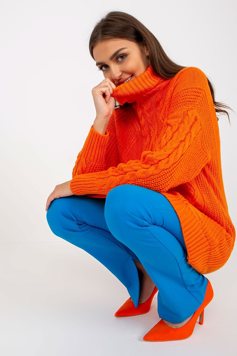 Luxurious Rue Paris Women's Long Turtleneck Jumper in striking orange, elegantly posed with blue trousers, exuding sophistication and style.