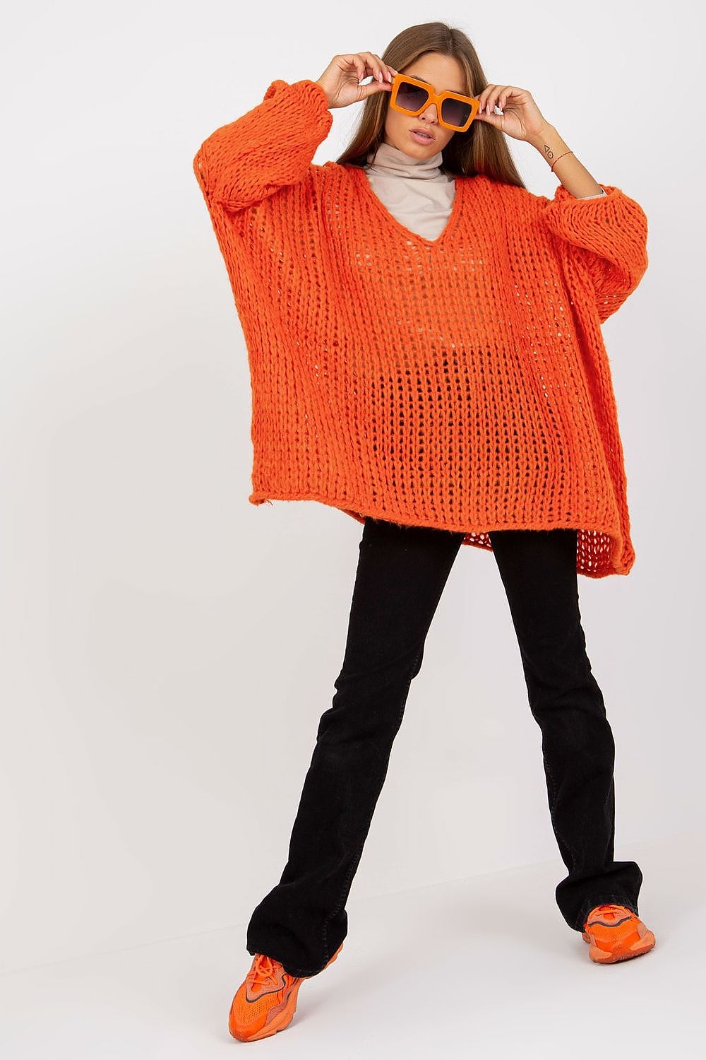 Luxury Women's Loose Fit Sweater With Heart Neckline & Asymmetrical Hem By Och Bella displayed in vibrant orange, styled with wide long sleeves, paired with black trousers and striking orange sunglasses for a chic look.