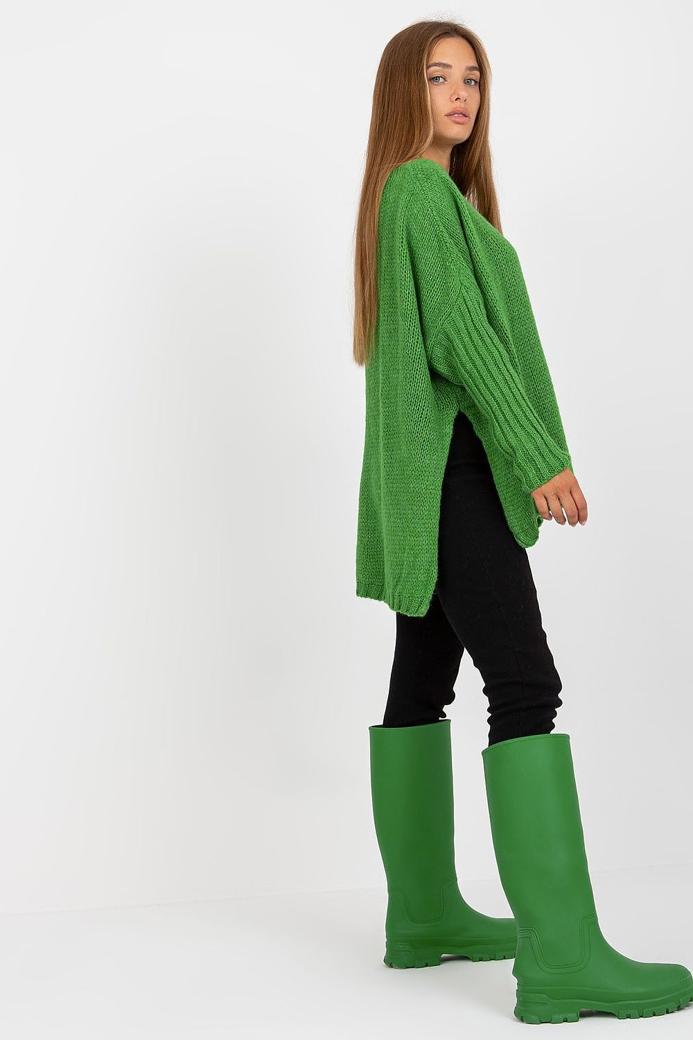 Engaging profile of a model in the Stylish Women's Loose Fit Sweater by Och Bella, featuring side slits, paired with vivid green rubber boots for a contemporary look.