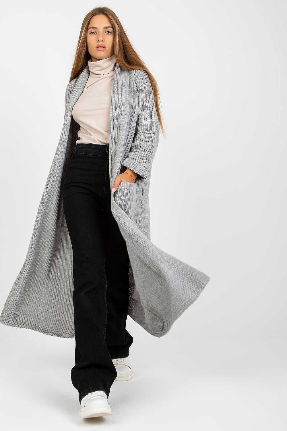 Model showcasing the Elegant Long Unbuttoned Cardigan by Och Bella, crafted from 70% acrylic and 30% wool, featuring sleek slip pockets, paired with stylish black trousers and white sneakers.