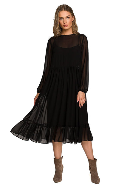 Sophisticated woman wearing a black chiffon cocktail dress with ruffled hem and wide sleeves, radiating elegance in a luxurious evening setting.