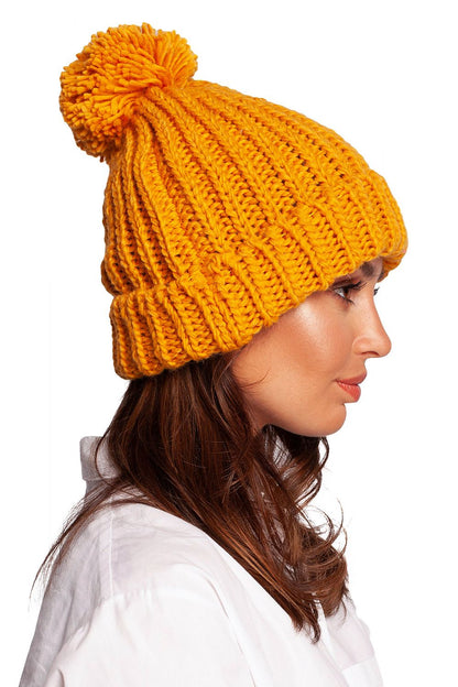 Profile view of a luxurious orange pom-pom beanie hat showcasing its knitted texture, ideal for stylish winter outings.