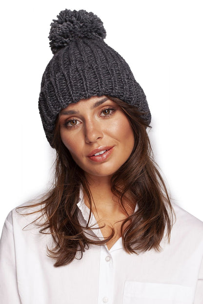 Elegant dark grey pom-pom beanie hat, elegantly worn by a model in a white blouse, perfect for cold weather chic.