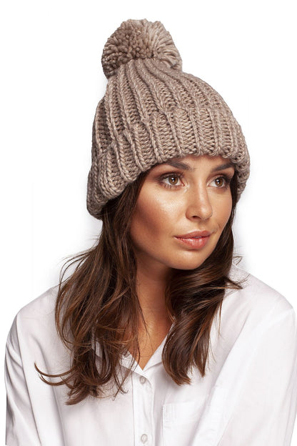 Chic beige pom-pom beanie hat displayed on a model, radiating luxury and comfort, ideal for complementing winter attire.