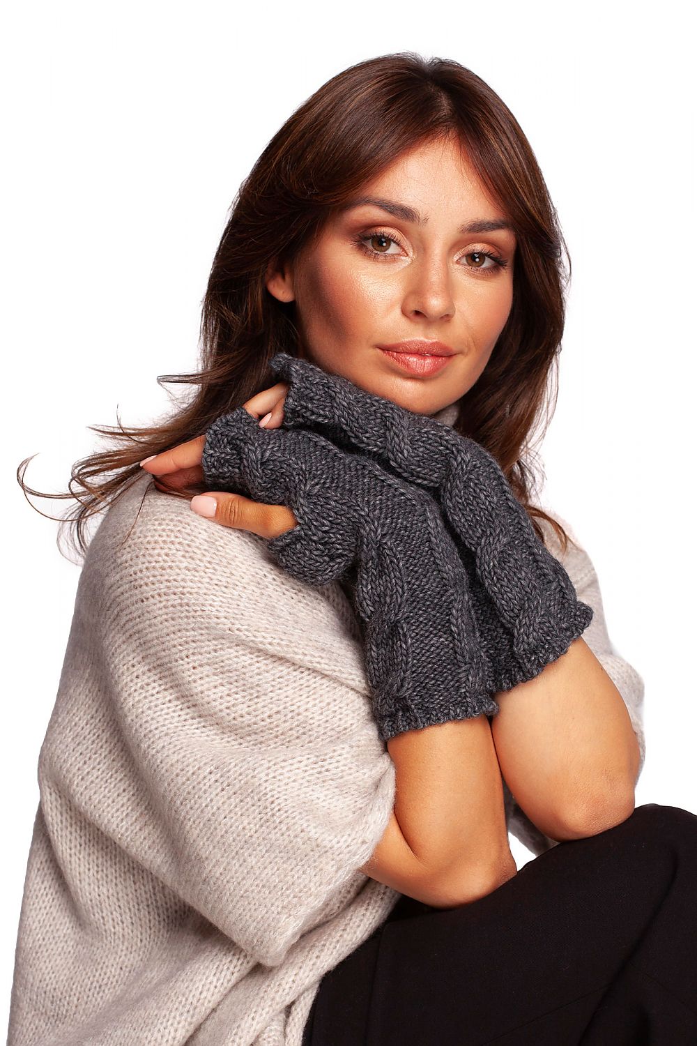 Sophisticated woman wearing chic grey fingerless gloves, elegantly posed against a soft knit backdrop.