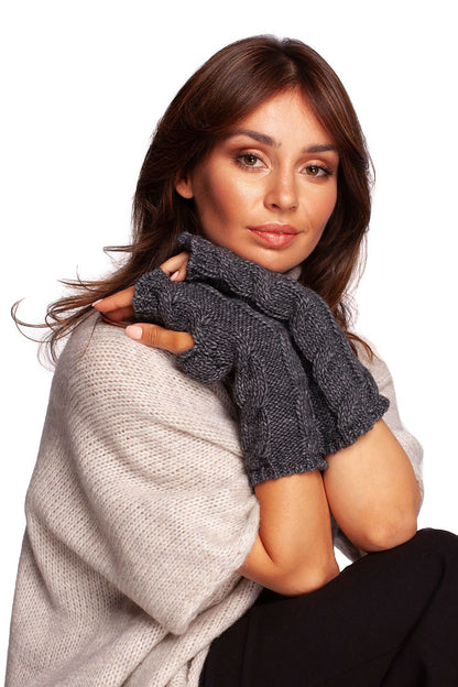Sophisticated woman wearing chic grey fingerless gloves, elegantly posed against a soft knit backdrop.