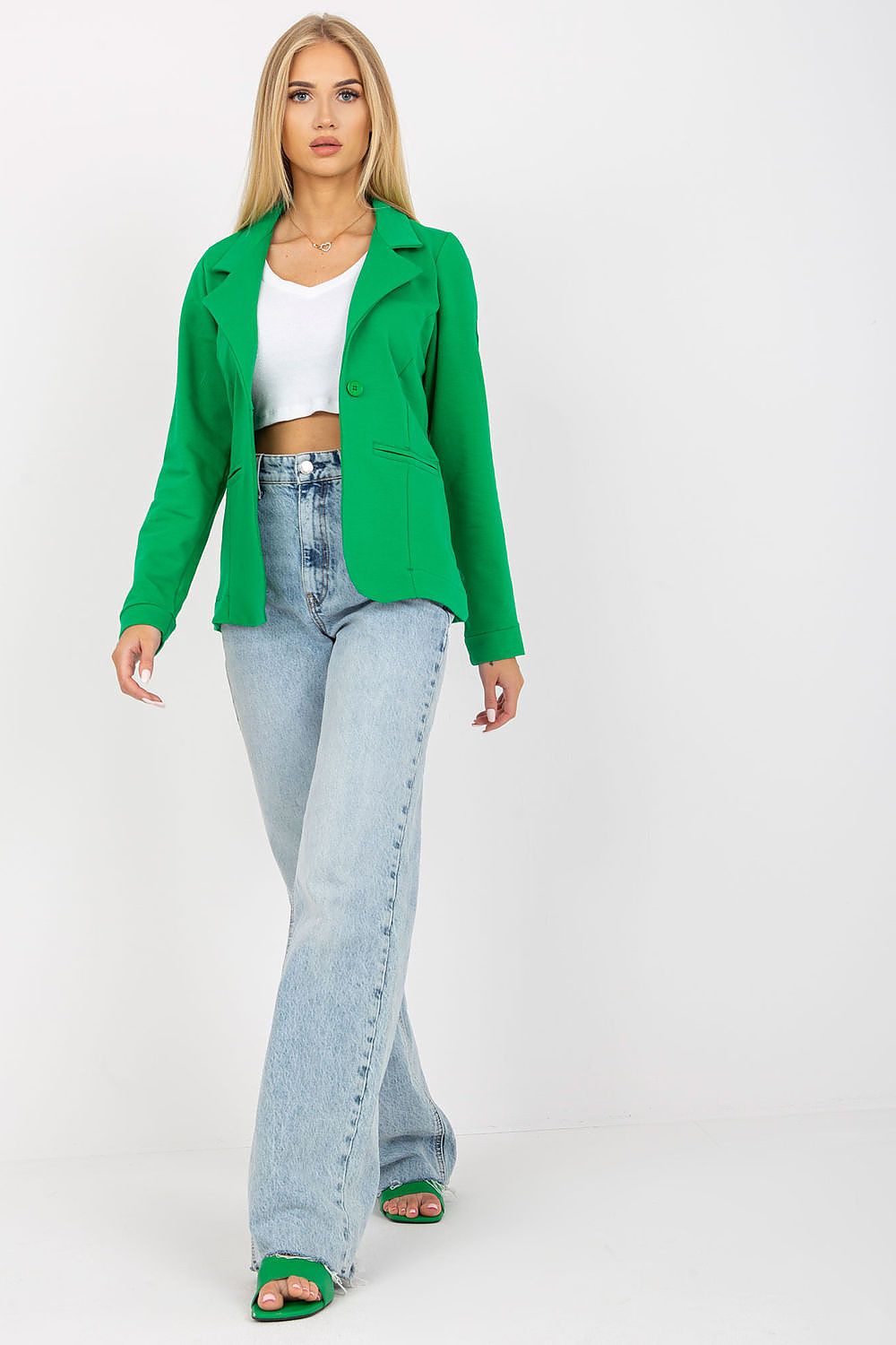 Stylish outfit presentation featuring a long sleeve green jacket by Och Bella, model striding confidently in flared light blue jeans and vibrant green heels, embodying luxury and elegance.