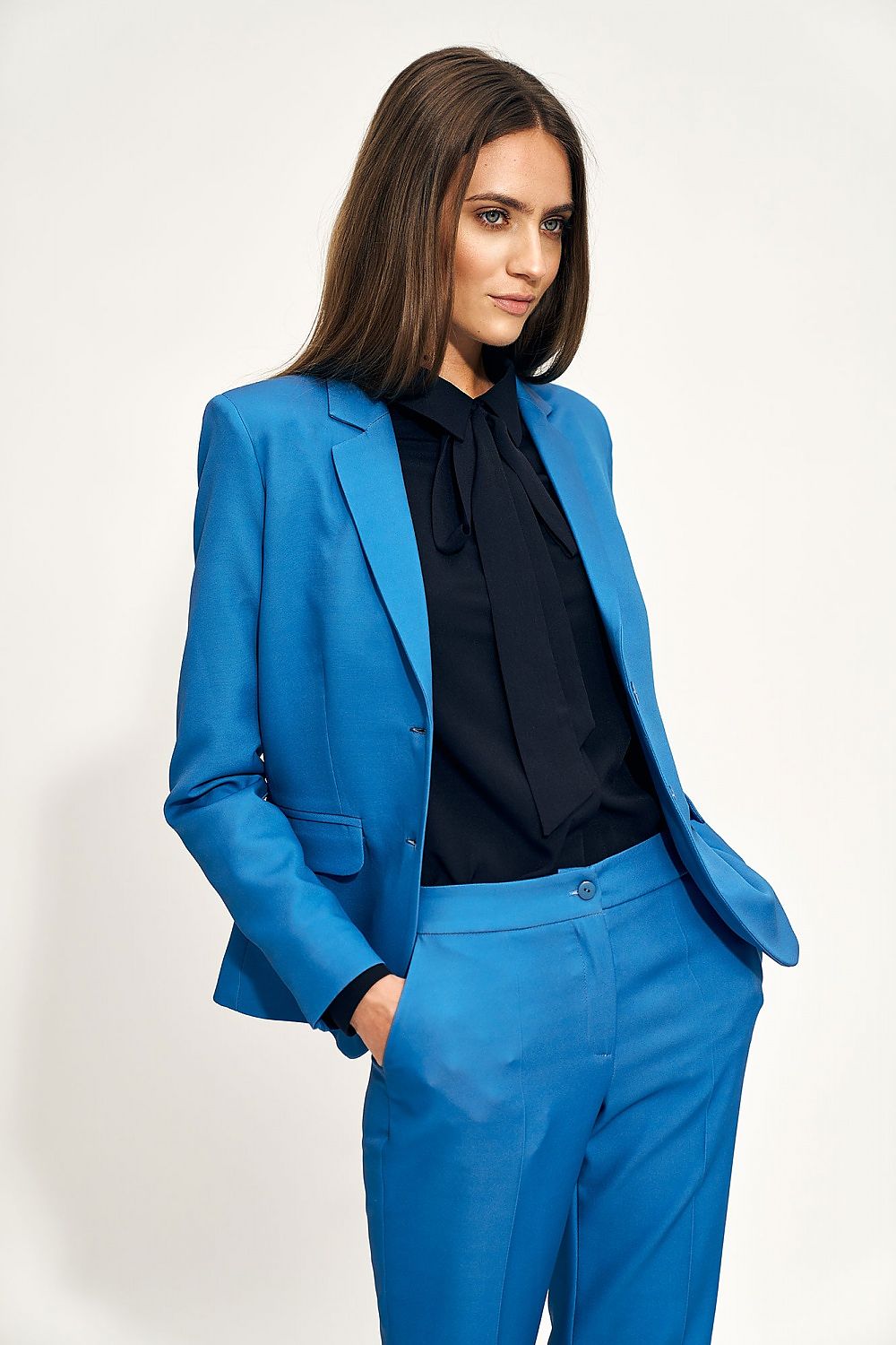 Model exuding sophistication in a black Nife blouse with bow detail and a striking blue suit jacket, embodying luxurious office attire.