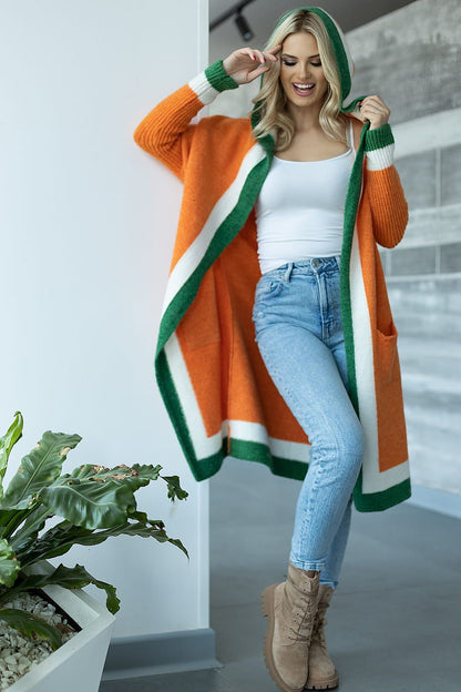 Chic loose cardigan with hood and contrasting slip pockets in rich orange and green hues, elegantly styled on a smiling woman, showcasing a trendy fashion look in a sleek indoor setting.