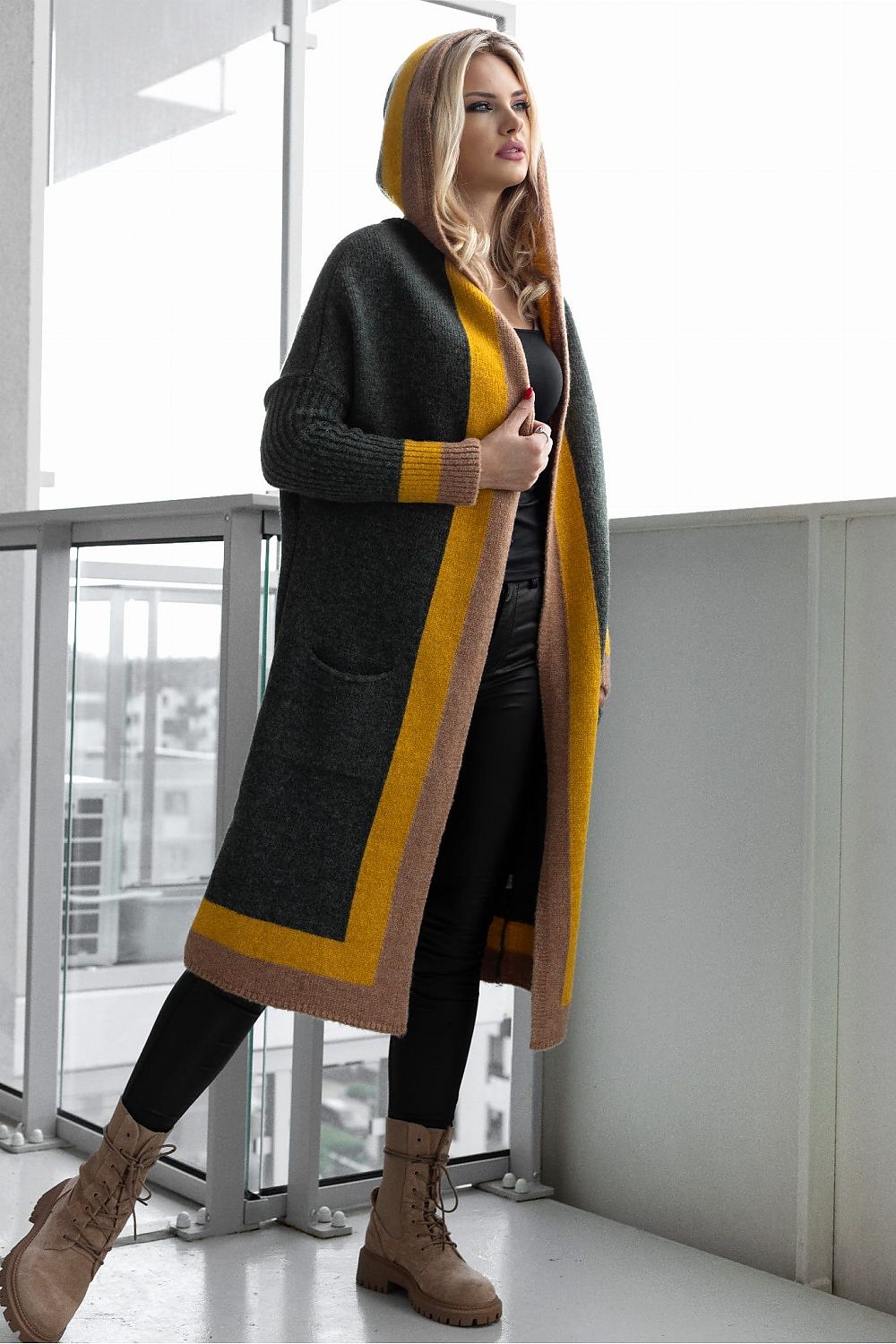 Elegant loose cardigan with hood in a rich colour palette, featuring soft fluffy fabric and slip pockets, showcased by a model against a modern architectural backdrop.