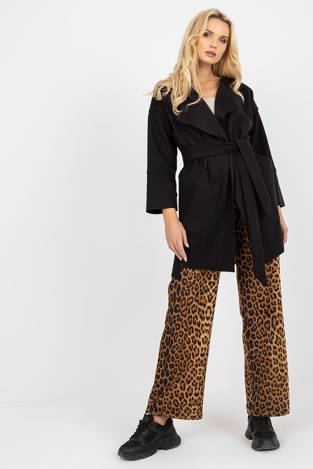 Chic front view of a woman donning a black slim fit coat with an open front design and tie belt, complemented by animal print wide-leg trousers.