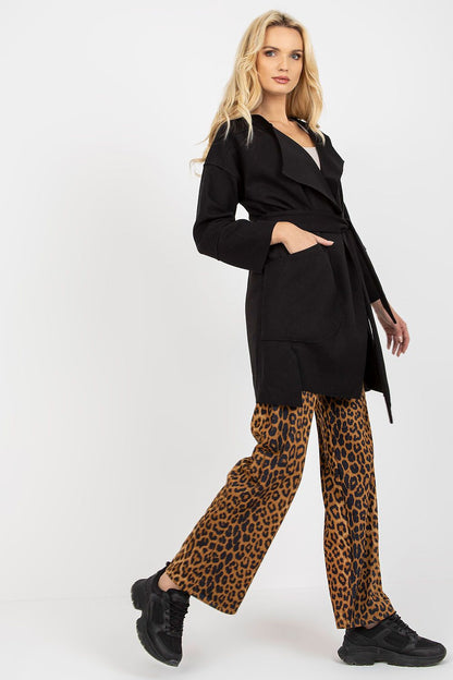 Stylish side view of a woman showcasing a black slim fit coat tied at the waist, adorned with spacious patch pockets and contrasting leopard print pants.