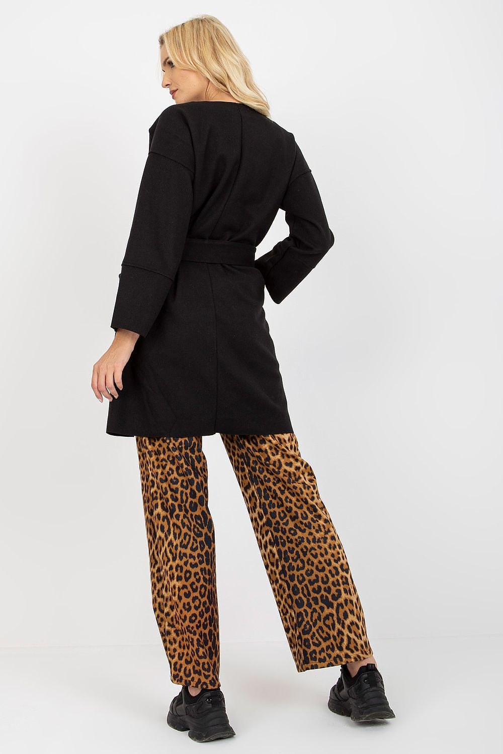 Sophisticated rear view of a woman in a black slim fit coat with a tie belt, paired with trendy leopard print trousers, highlighting a fashionable silhouette.