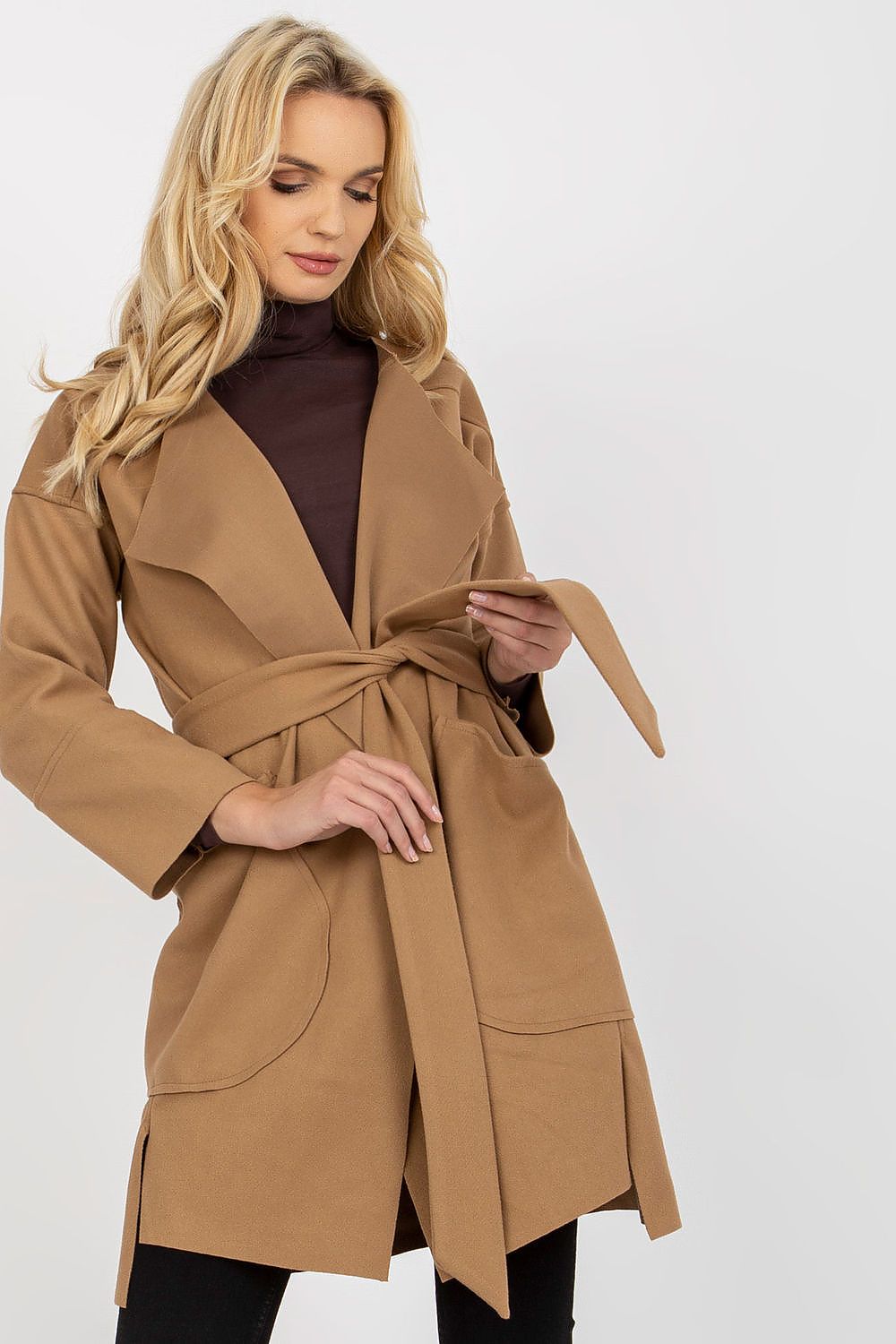 Charming front view of a woman in a brown slim fit coat with a tie belt, displaying oversized pockets and a stylish layered look with a brown turtleneck underneath.