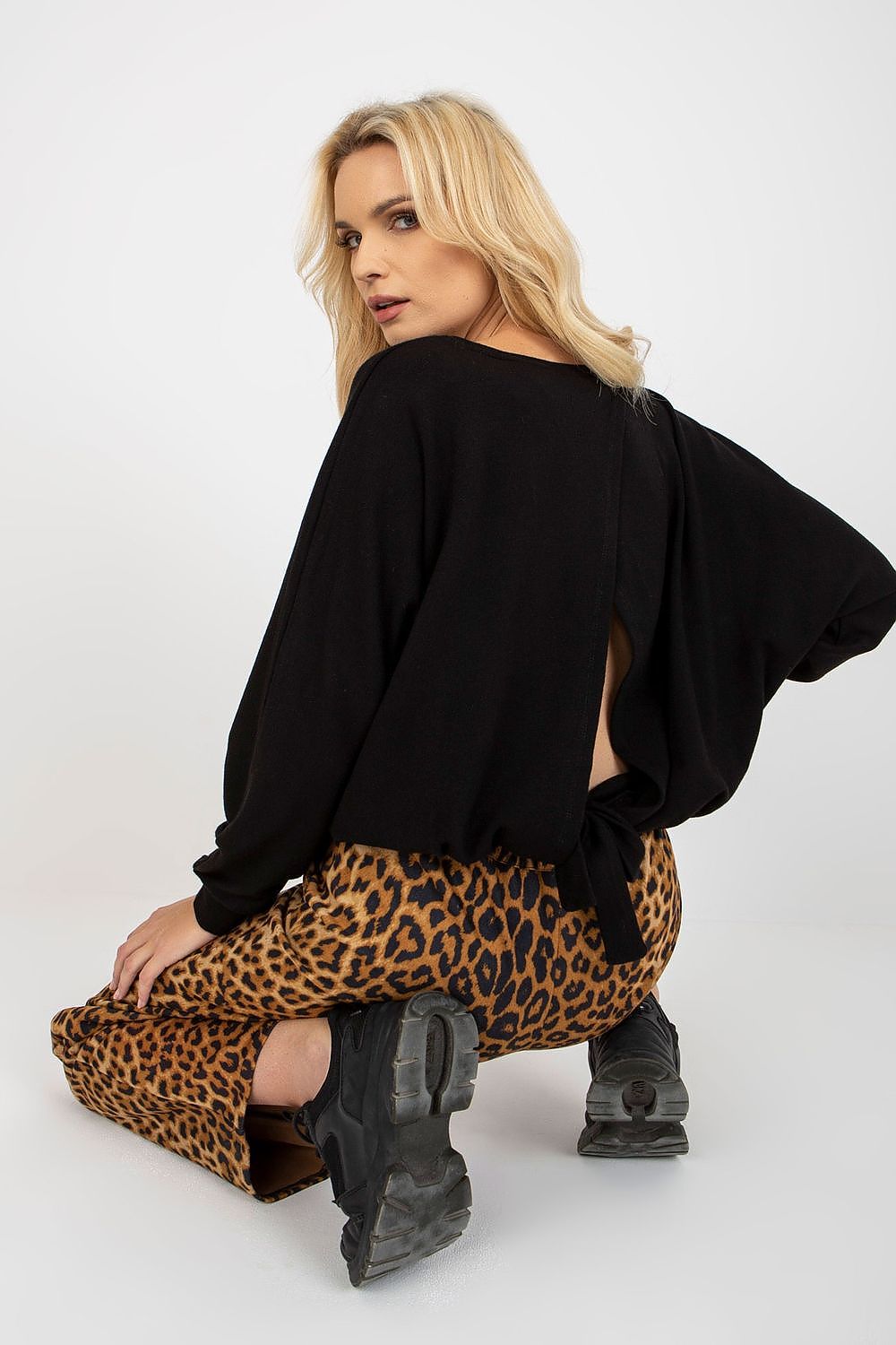 Luxury back view of a black women's sweater with a stylish slit and decorative binding, paired with fashionable leopard print bottoms.