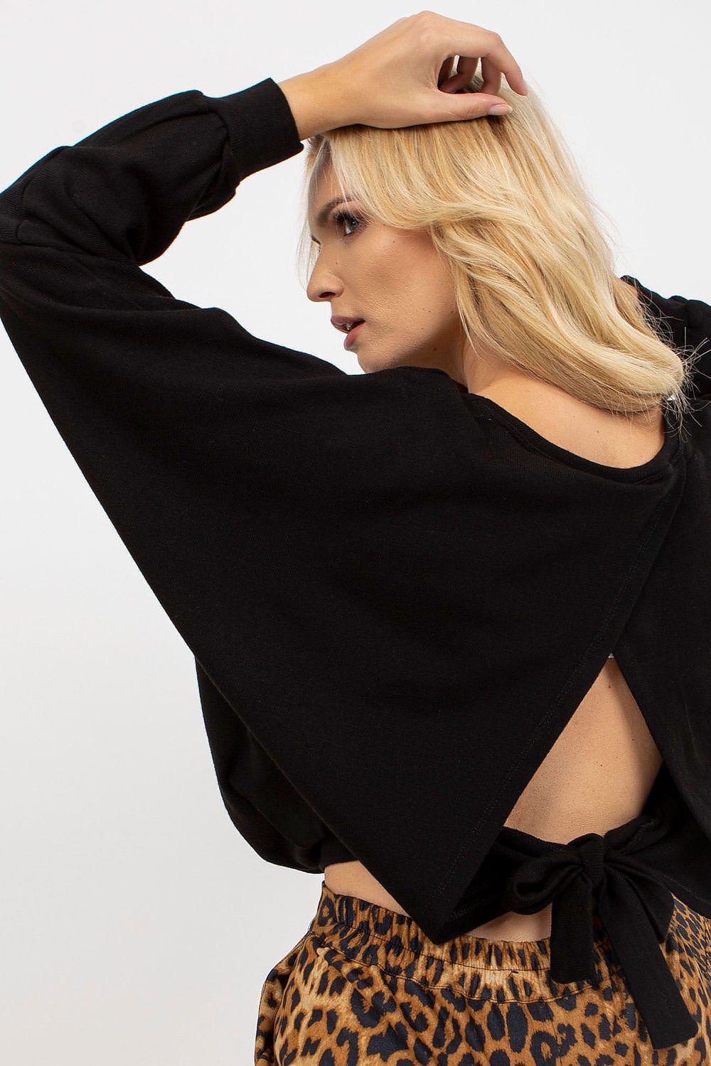 Chic women's black sweater showcasing a unique back design with a tied detail, complemented by trendy leopard print pants.