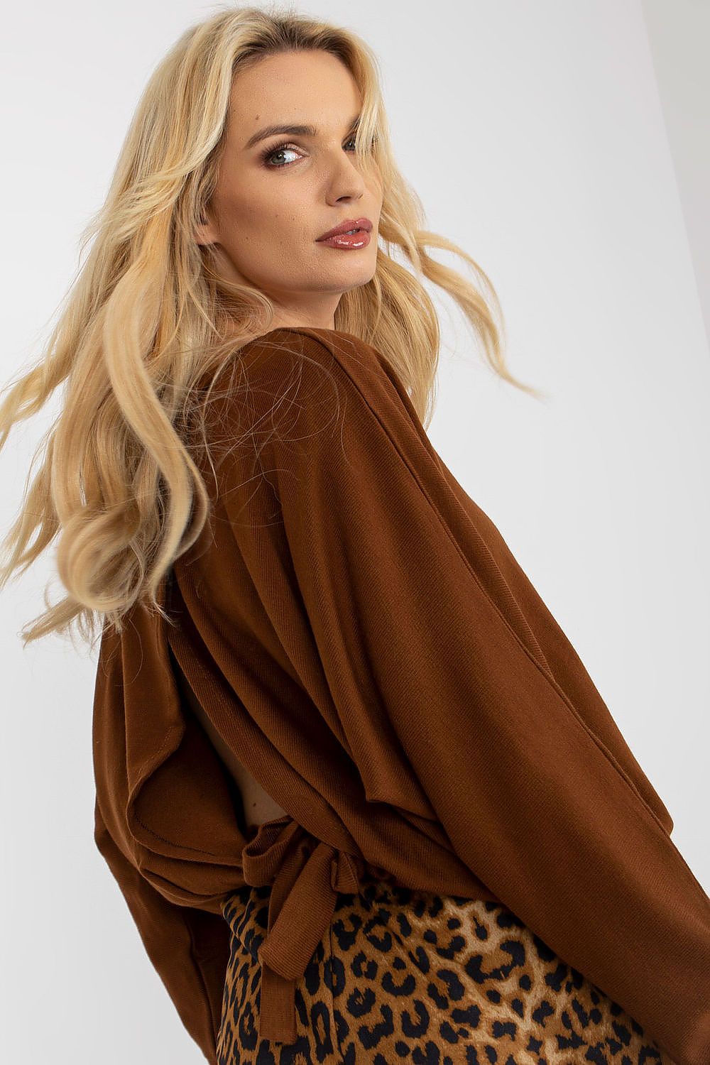Elegant woman showcasing a luxury brown oversized women's sweater with a boat neckline and slit back design, styled with a chic animal print skirt, perfect for a sophisticated wardrobe.