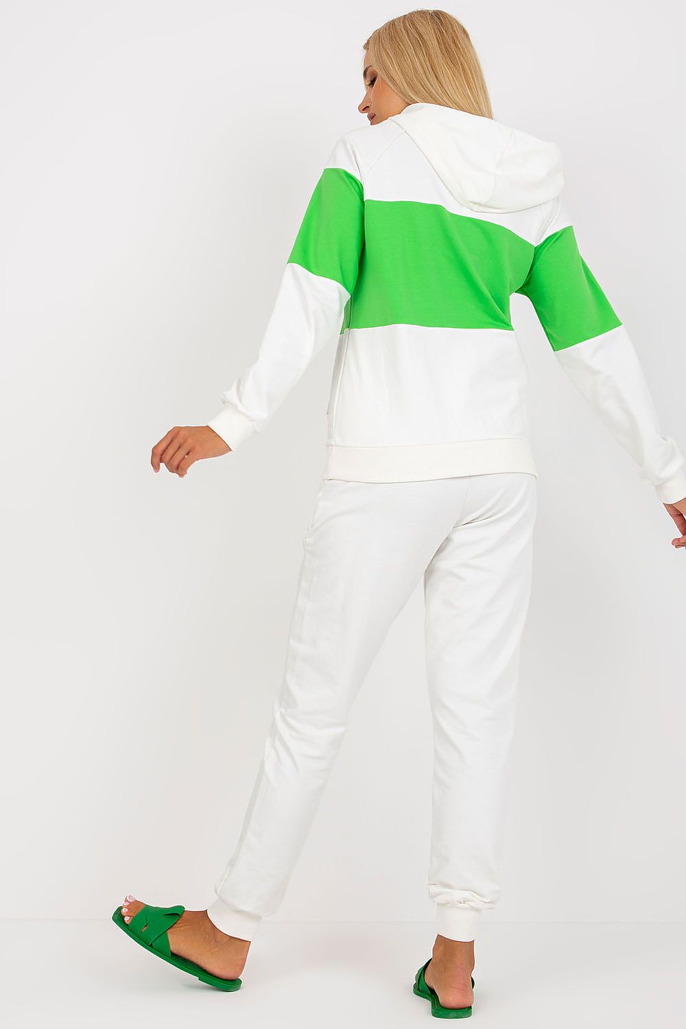 Fashionable back view of a woman in a white and green luxury cotton blend sweat outfit, emphasizing the elegant hoodie and fitted pants, complemented with trendy green footwear.