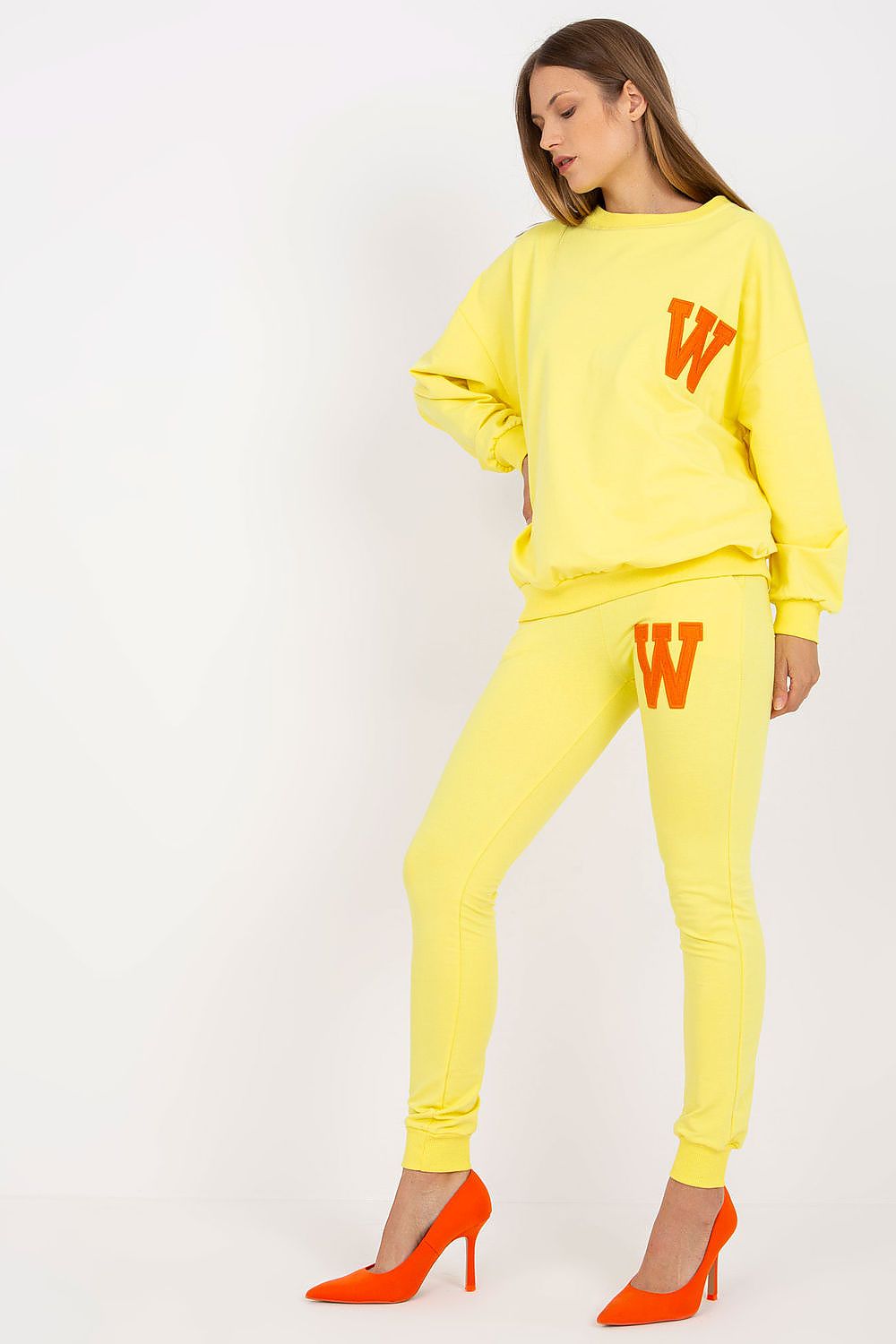 Chic yellow cotton-spandex sweatsuit set featuring a loose cut sweatshirt with vibrant orange patch and coordinating long pants, styled with elegant orange high heels, perfect for a fashionable casual look.