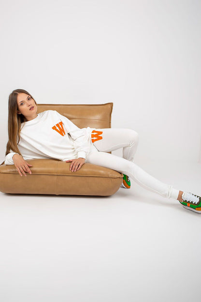 Elegant model lounging in a stylish white sweatsuit set, adorned with vibrant orange 'W' patches, showcasing a luxurious blend of comfort and chic fashion.