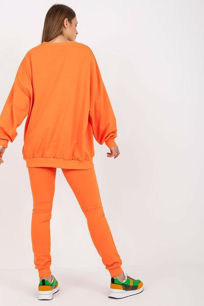 Rear view of a stylish model wearing an orange sweatsuit set, highlighting the loose-cut sweatshirt and fitted long pants, styled with fashionable athletic shoes.