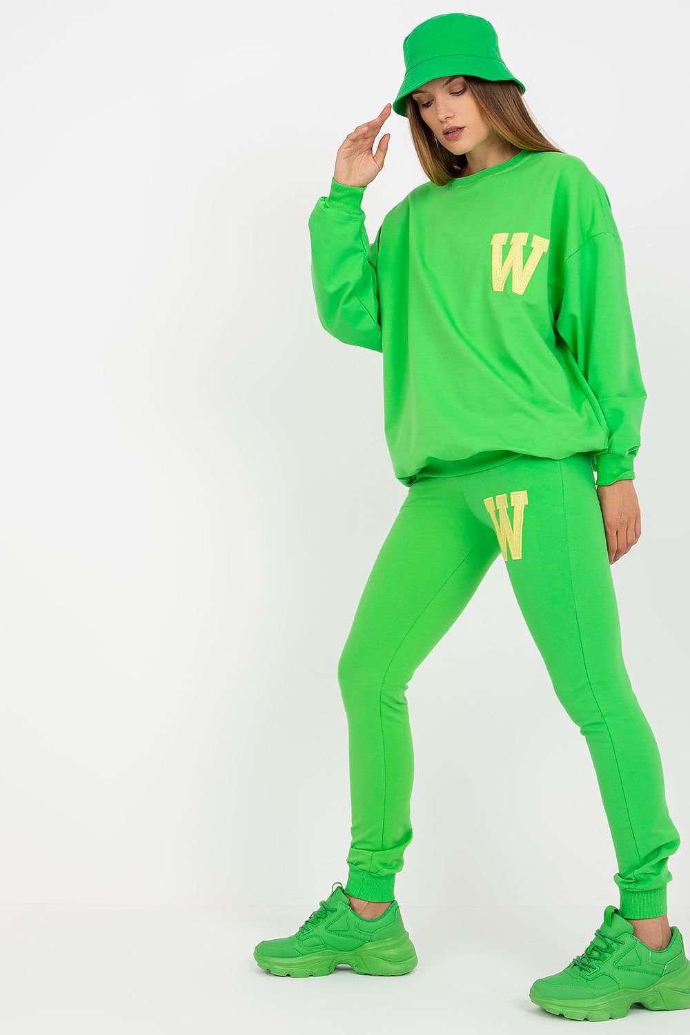 Fashion-forward model showcasing a green sweatsuit with a decorative patch, complete with a bucket hat and chic sneakers, exuding luxury and comfort.