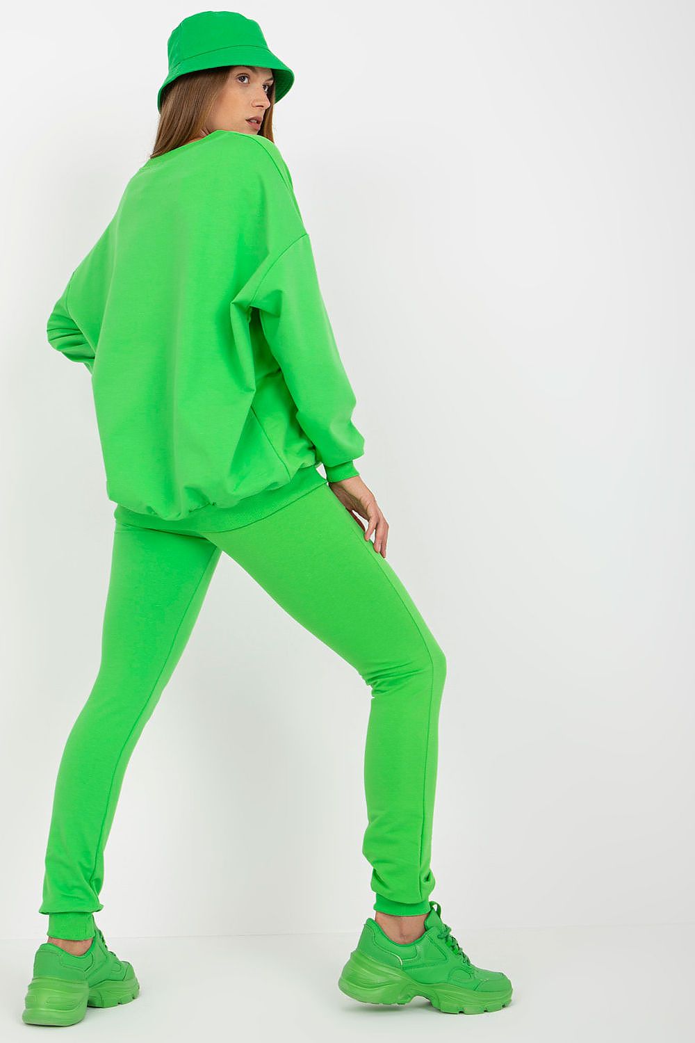 Sophisticated rear view of a model in a matching green sweatsuit set with fitted long pants and a loose-cut top, paired with stylish sneakers, radiating elegance.