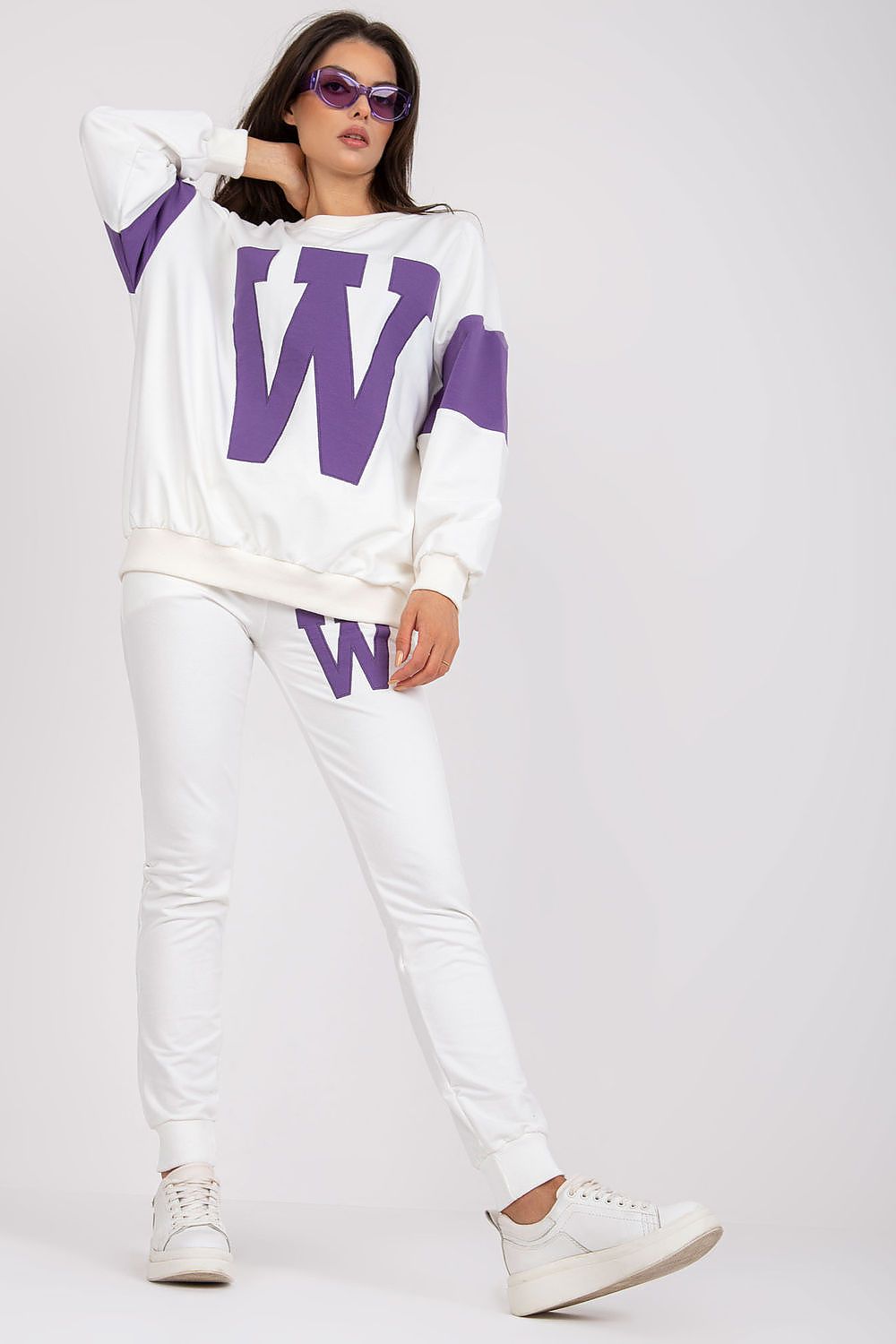 Stylish women's tracksuit in luxurious white fabric, featuring a purple 'W' logo on a loose-cut sweatshirt and matching tailored pants, completed with sporty white sneakers for an effortless look.