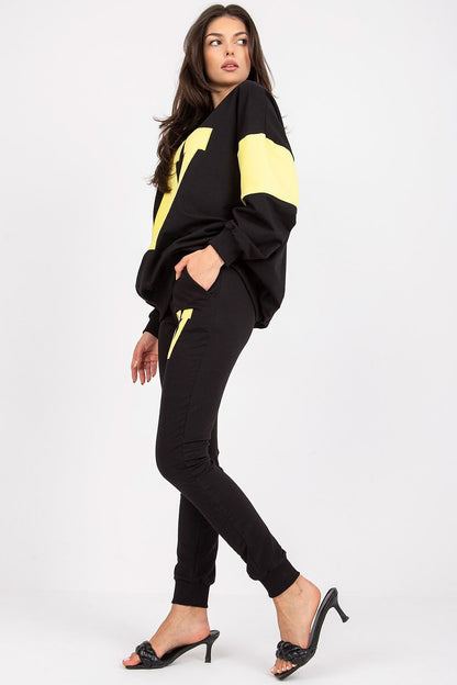 Elegant luxury women's black tracksuit set featuring a loose cut sweatshirt with yellow accents, paired with tailored pants. Model showcases a fashionable side view, accentuating comfort and style.