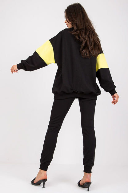 Chic luxury women's black tracksuit set displayed from the back, highlighting the oversized sweatshirt with yellow detailing and tailored pants. Stylish model demonstrates a perfect blend of comfort and elegance.