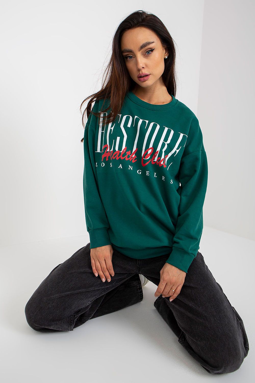 Elegant green long-sleeved cotton sweatshirt with decorative print, exuding casual refinement, elegantly posed on knees against a minimalist backdrop.