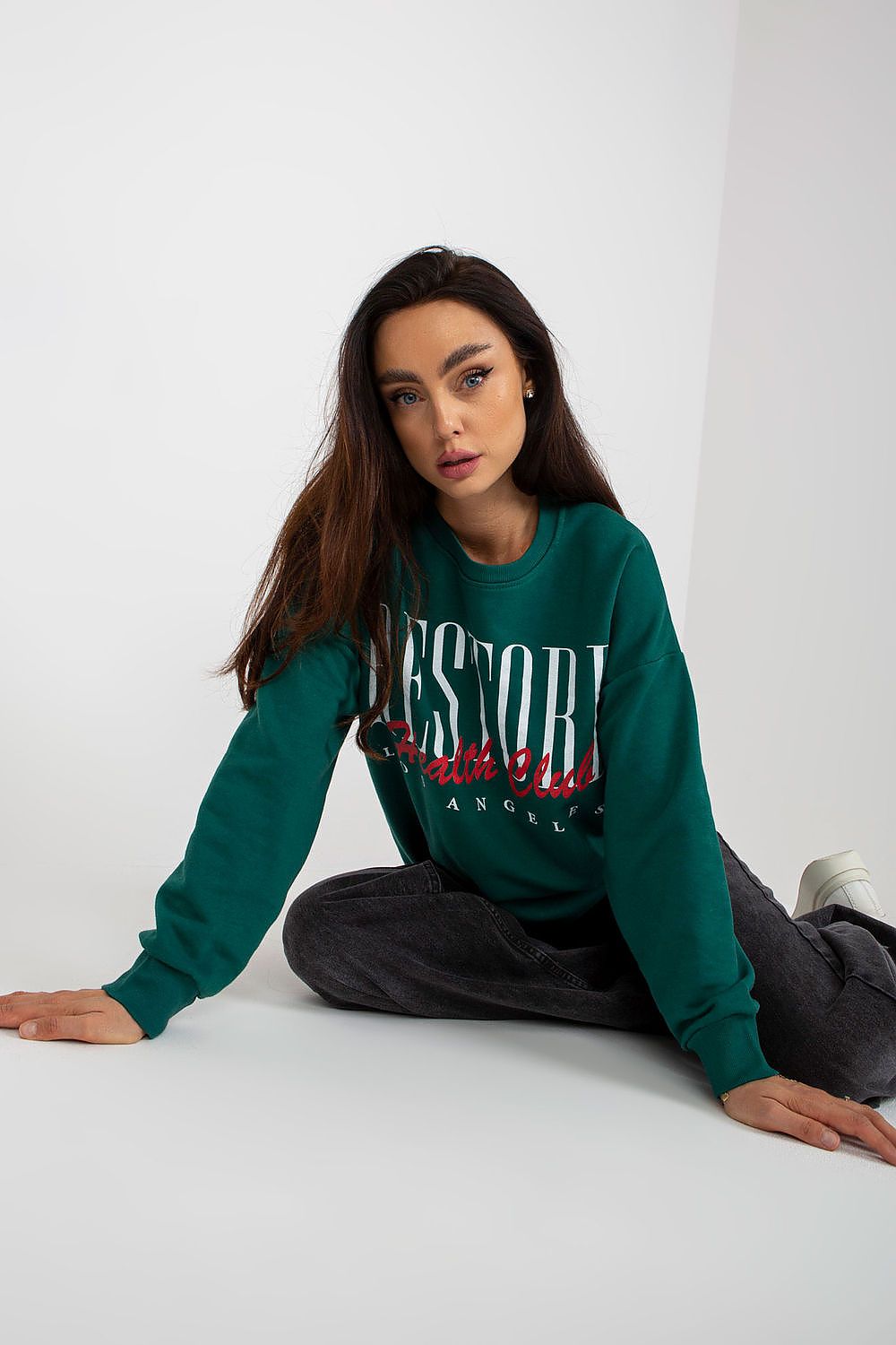 Elegant long-sleeved 100% cotton sweatshirt in a deep green hue, featuring a decorative print, styled casually with dark jeans for a chic yet comfortable look.
