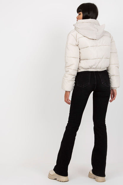 View from behind of a fashionable model wearing a cream quilted jacket with a hood, highlighting the sleek design and stylish cut, paired with black flared jeans.