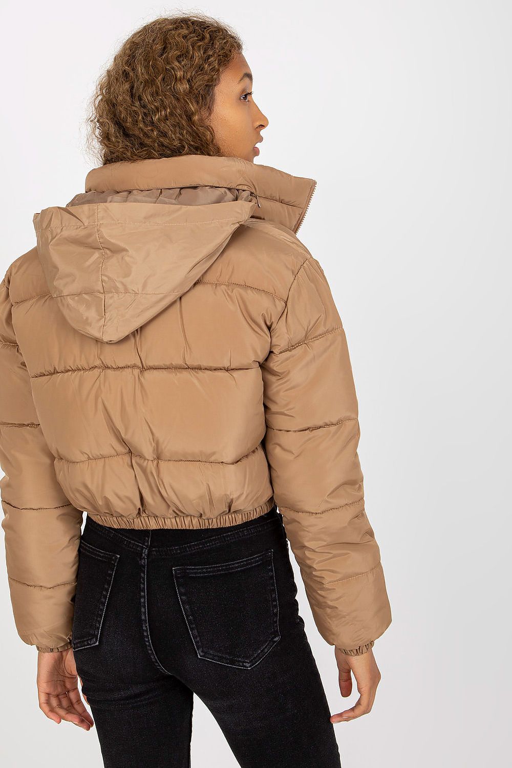 Back view of a fashionable model in a stylish brown quilted jacket with a non-removable hood, emphasising the sleek silhouette and paired with tailored black jeans.