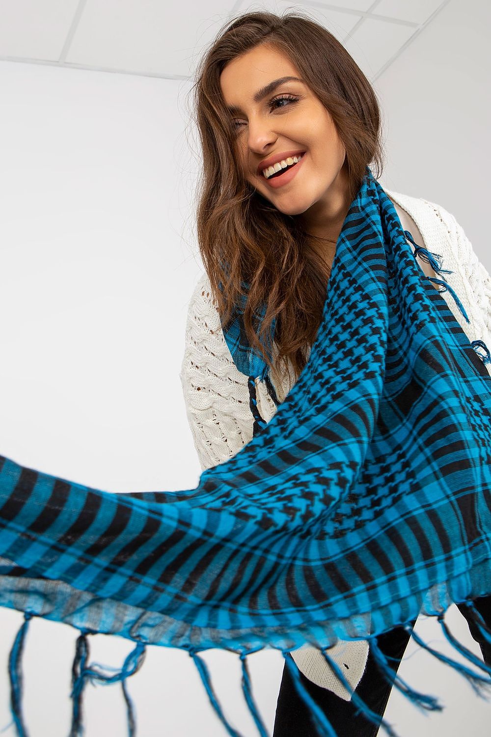 Radiant model smiling while showing off a luxurious blue checkered neckerchief scarf, full of texture and vibrancy, set against a simple backdrop to accentuate the accessory.