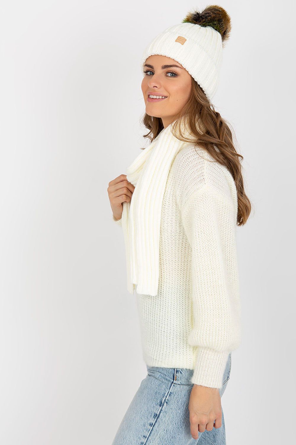 Profile view of a sophisticated woman showcasing a cream winter hat with a pom pom and a coordinating scarf, perfect for chic winter outings.