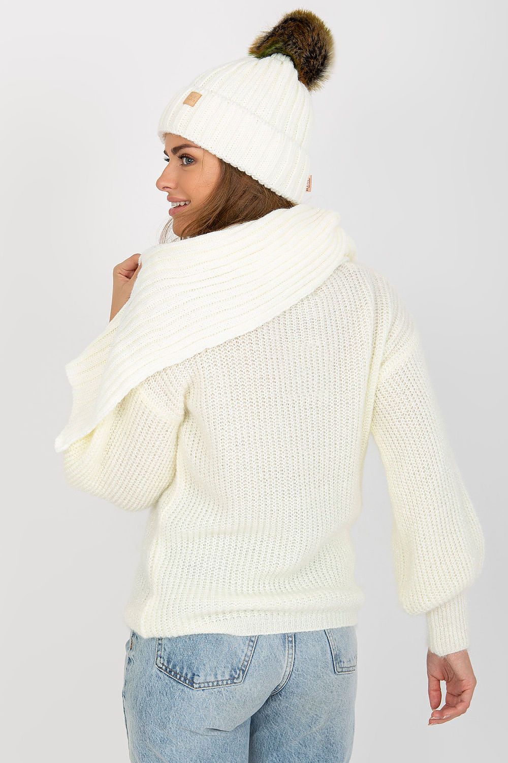 Back view of a fashionable woman displaying her cream winter accessories, including a knitted hat and scarf, ideal for a stylish winter wardrobe.
